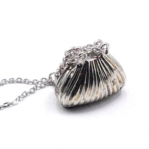 May include: A silver chain necklace with a small, silver, purse-shaped pendant. The pendant has a ribbed texture.