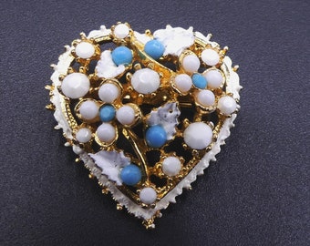 Puede incluir: Un broche de corazón de oro con esmalte blanco y piedras de vidrio azul. El broche está decorado con un diseño floral.