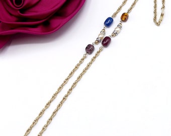 May include: Gold-tone necklace with a rope chain design. The necklace features a series of colorful beads, including blue, amber, purple, and red, interspersed with small pearls. A fuchsia fabric rose is in the background.