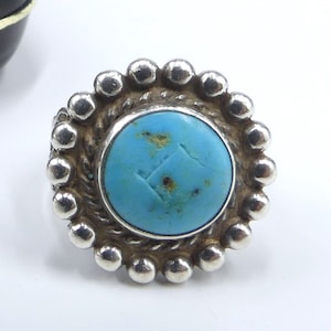 May include: A silver ring featuring a turquoise stone set within a beaded bezel. The stone has a light blue hue and a slightly rough surface.