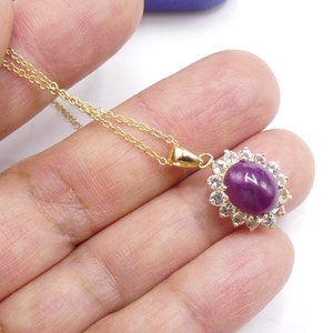May include: A gold chain necklace with a pendant featuring a large oval-shaped purple gemstone surrounded by a halo of smaller clear gemstones.