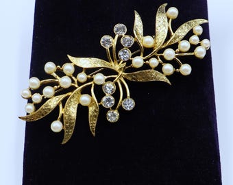 Puede incluir: Un broche de tono dorado con un diseño floral que presenta cuentas de imitación de perlas y diamantes de imitación transparentes.