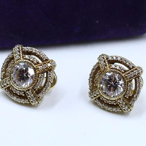 May include: A pair of gold earrings with a round, clear stone set in a decorative, multi-layered design.