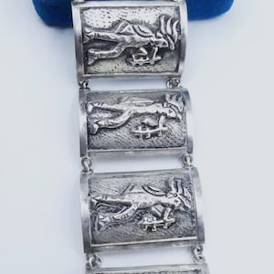 May include: A silver bracelet with six rectangular links, each featuring a detailed embossed design of a stylized figure. The bracelet has a clasp with a small tag that reads "STERLING MEXICO".
