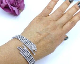 May include: A silver bracelet with multiple rows of clear rhinestones. The bracelet is designed with a unique, angled, open-ended design.