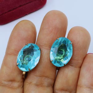 Op de afbeelding: Een paar vintage clip-on oorbellen met ovale, turquoise blauwe glazen stenen.