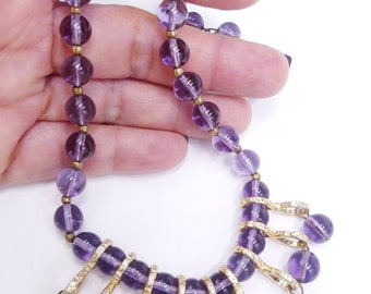 May include: A purple glass beaded necklace with a gold pendant featuring a cluster of dangling purple glass beads.