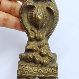 以下が含まれることがあります： 複雑な花柄と質感のある表面を持つヴィンテージの真鍮製装飾金具。2つの穴と詳細な装飾的なデザインがあります。