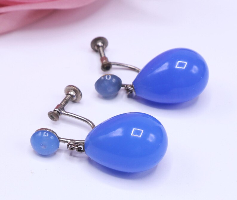 K&ouml;nnte beinhalten: Ein Paar Vintage-Ohrringe in Tropfenform in Blau mit silberfarbenen Metallbeschl&auml;gen. Die Ohrringe haben einen Schraubverschluss und einen kleinen blauen Perlenakzent. Der tropfenf&ouml;rmige Hauptk&ouml;rper der Ohrringe ist ein leuchtendes, gl&auml;nzendes Blau.