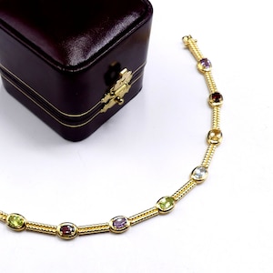 May include: A gold bracelet with a chain design and oval-shaped gemstones in various colors, including green, purple, red, and white.