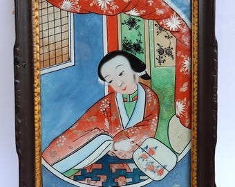 May include: A framed painting depicting a woman in a red and green robe seated in a room with a blue wall and a window. The woman is holding a fan and looking down at something in her lap.
