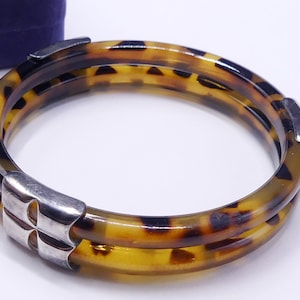 Könnte beinhalten: Ein doppelreihiges Armreif-Armband mit Schildpattmuster und silbernen Akzenten.