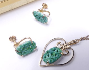 Pode incluir: Um conjunto de colar e brincos de jade verde. O pingente tem a forma de um coração com um design talhado. Os brincos são do tipo clip.