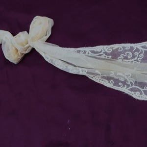 May include: A white lace scarf with a delicate floral pattern. The scarf is tied in a knot in the center.