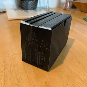 Op de afbeelding: Een zwarte doos met een stapel van vier boeken erin. De boeken hebben gouden letters op de ruggen. De doos heeft een ontwerp van vier gestileerde potloden aan de voorkant.