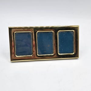 May include: A rectangular gold-toned metal picture frame featuring three vertical openings for photographs. The frame has a polished, reflective surface and a smooth, continuous border surrounding each of the three dark blue display windows.