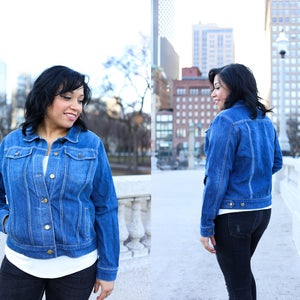 May include: A woman wearing a blue denim jacket over a white t-shirt and black jeans. She is standing in front of a city background.