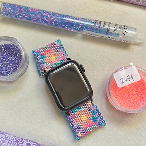 May include: A black smartwatch with a custom beaded watch band featuring a floral pattern in pink, blue, and yellow. Included are three containers of seed beads: one tube labeled Miyuki Drop 3.4mm Electric, and two small jars labeled 694 and 2034.