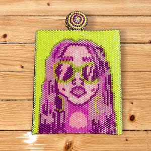 Peut inclure: Portrait perlé d'une femme aux cheveux roses et aux lunettes de soleil, sur fond vert citron. L'œuvre est encadrée en noir et comporte un dessus perlé assorti. Le portrait est fait de petites perles roses, violettes et jaunes.