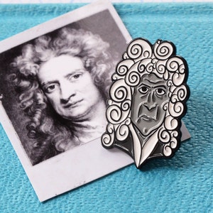 May include: A black and white enamel pin depicting a stylised portrait of Isaac Newton with a curly wig. The pin is on a blue surface.