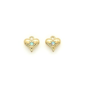 May include: Two gold-colored heart-shaped charms with a small, light blue gemstone in the center. The charms have a textured surface and a loop at the top for hanging. The background is plain white.