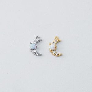 Puede incluir: Dos dijes de media luna con una piedra de ópalo blanco y detalles de cristal transparente. Un dije es plateado y el otro es dorado.