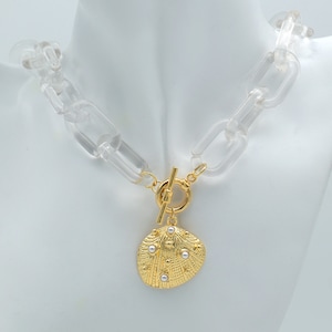 May include: A clear acrylic chain necklace with a gold-tone seashell pendant accented with white pearls.