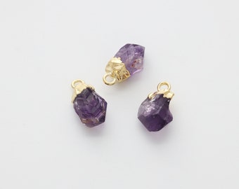 Puede incluir: Tres pequeños colgantes de cristal de amatista con detalles en metal dorado. Los cristales son de color morado oscuro y tienen una textura rugosa y natural.