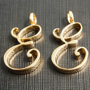 May include: Two gold-colored, cursive letter E charms. The charms are made of metal and have a shiny finish.