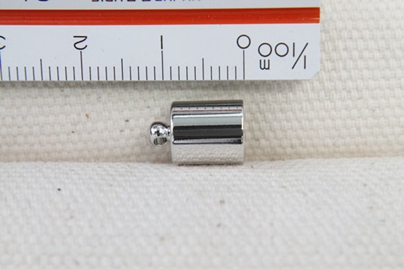Op de afbeelding: Zilveren metalen eindkap voor koord of touw. De eindkap is ongeveer 1,2 cm lang en heeft een afgerond uiteinde.