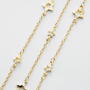 May include: Three gold chains with open star charms. The chains are layered and the stars are of varying sizes.