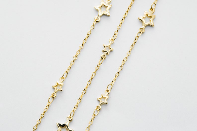 May include: Three gold chains with open star charms. The chains are layered and the stars are of varying sizes.