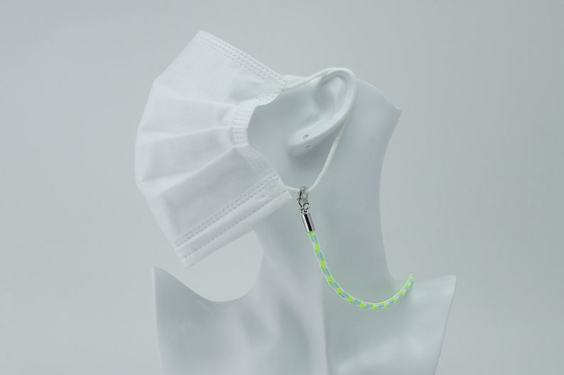 May include: A white face mask with a green and white lanyard. The lanyard has a silver clasp.