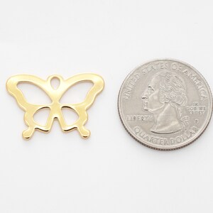 Puede incluir: Un dije de mariposa de metal dorado, que se muestra junto a una moneda de veinticinco centavos de d&oacute;lar estadounidense para comparar el tama&ntilde;o.