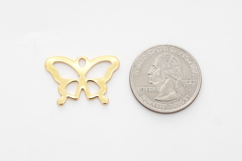 Puede incluir: Un dije de mariposa de metal dorado, que se muestra junto a una moneda de veinticinco centavos de d&oacute;lar estadounidense para comparar el tama&ntilde;o.