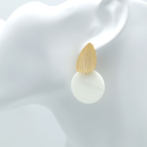 Puede incluir: Pendientes colgantes geométricos dorados y blancos. Los pendientes tienen una pieza dorada en forma de lágrima y una pieza redonda blanca.