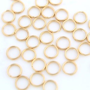 Pode incluir: Uma grande quantidade de argolas de salto douradas, que são pequenas argolas de metal usadas para conectar componentes de joias.