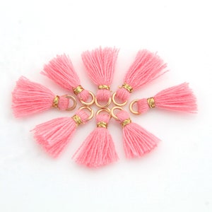 May include: Eight pink tassels with gold rings. The tassels are arranged in a circle on a white background.