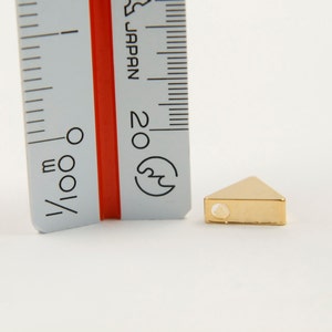 May include: A gold triangle-shaped bead with a hole in the centre. The bead is approximately 1 cm wide and is shown next to a ruler.