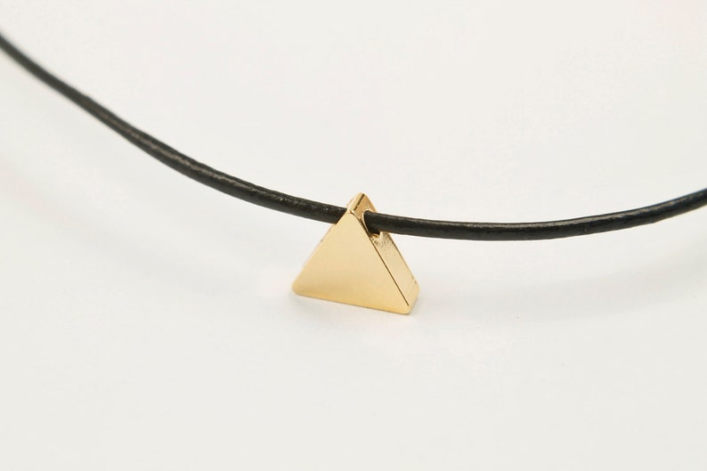 May include: A gold triangle pendant necklace on a black leather cord.