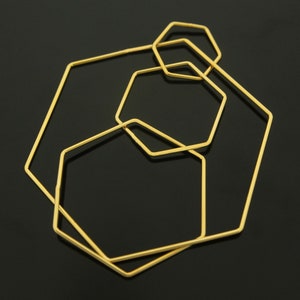 May include: Four gold-colored hexagonal hoops of different sizes, nested inside each other, against a black background.