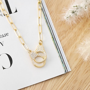 May include: A gold chain necklace with a pendant shaped like handcuffs, encrusted with clear rhinestones.