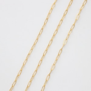 May include: Three gold chains with a delicate, oval-shaped link design. The chains are arranged in a diagonal pattern on a white background.