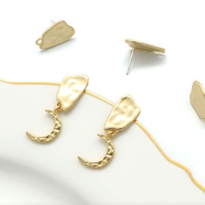 May include: A pair of gold-tone earrings with a crescent moon charm dangling from a textured, irregular-shaped pendant.