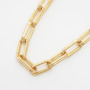 Puede incluir: Un collar de cadena dorado con eslabones rectangulares grandes. La cadena se muestra sobre un fondo blanco, resaltando su apariencia brillante y metálica. Esta joya es adecuada para diversas ocasiones.