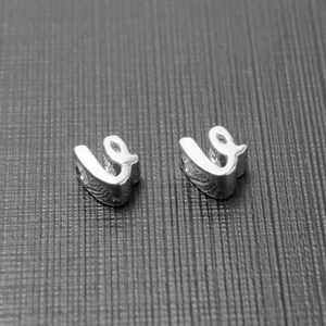May include: Two silver charms shaped like the letter "U" with a curved design.