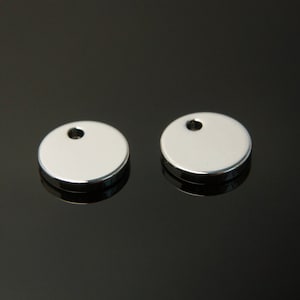 Op de afbeelding: Twee ronde zilveren metalen labels met een klein gaatje bovenaan.