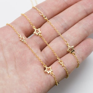 May include: Three gold chains with star-shaped pendants. The chains are layered on top of each other, with the shortest chain on top and the longest chain on the bottom.