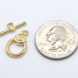 Peut inclure: Fermoir &agrave; bascule en m&eacute;tal dor&eacute; avec un motif en spirale. Le fermoir est pr&eacute;sent&eacute; &agrave; c&ocirc;t&eacute; d'un quart de dollar am&eacute;ricain pour comparaison de taille.