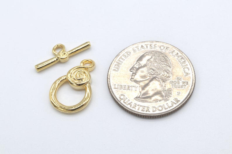 Peut inclure: Fermoir &agrave; bascule en m&eacute;tal dor&eacute; avec un motif en spirale. Le fermoir est pr&eacute;sent&eacute; &agrave; c&ocirc;t&eacute; d'un quart de dollar am&eacute;ricain pour comparaison de taille.